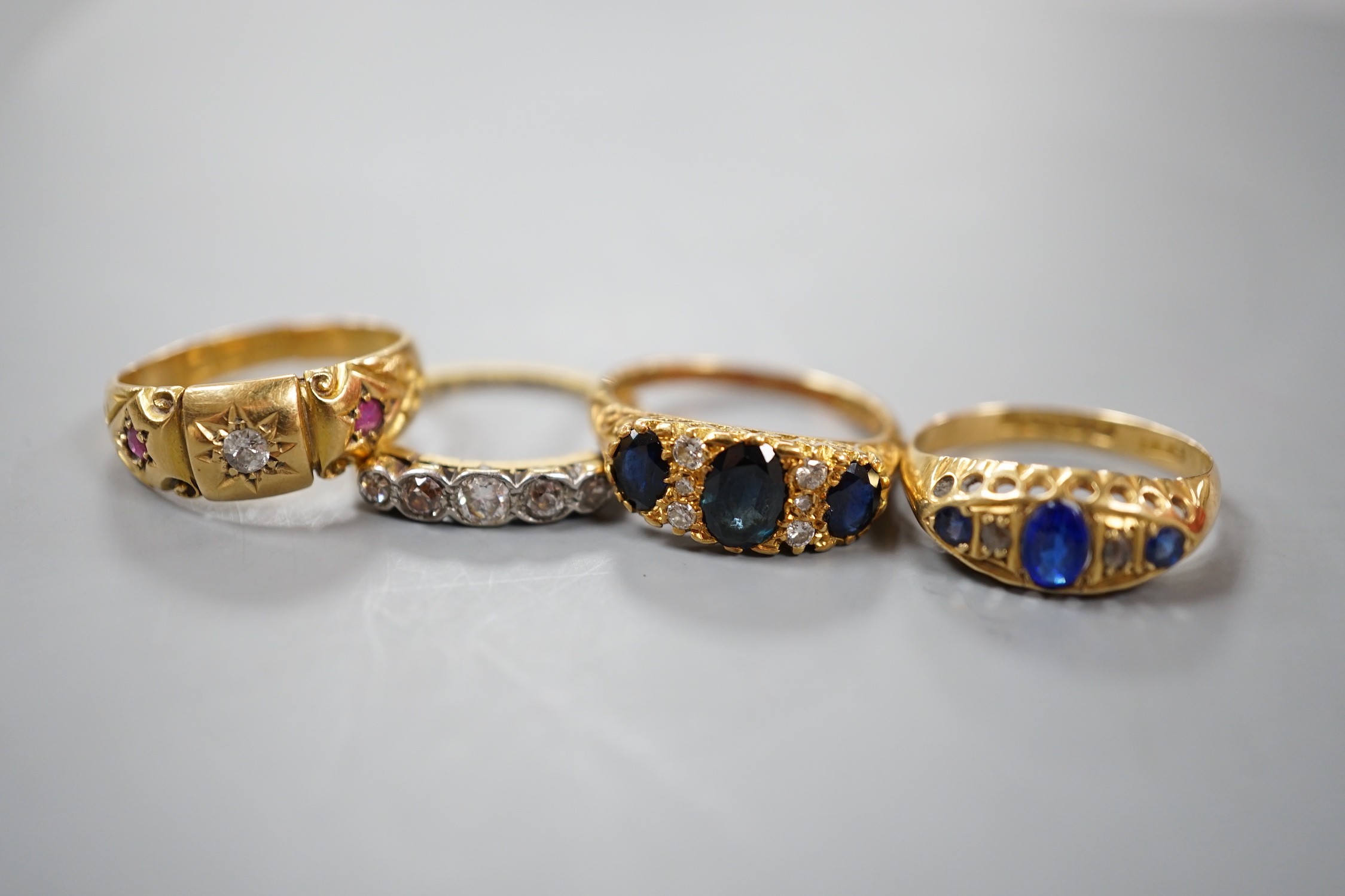 Three early 20th century 18ct and gem set half hoop rings, including ruby and diamond chip, five stone diamond, blue paste and blue stone doublet and diamond chip and a modern 18ct gold sapphire and diamond ring, gross w